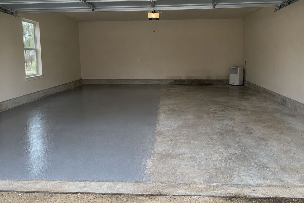 Ground concrete garage slab with a clear primer applied over half the floor and a darker damp-looking patch near the wall, in humid gray light
