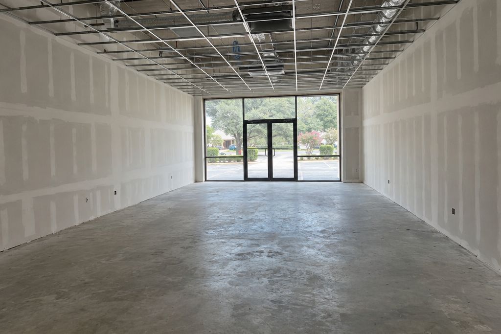 Empty commercial lease space with a bare ground concrete floor ready for coating, new drywall and a ceiling grid