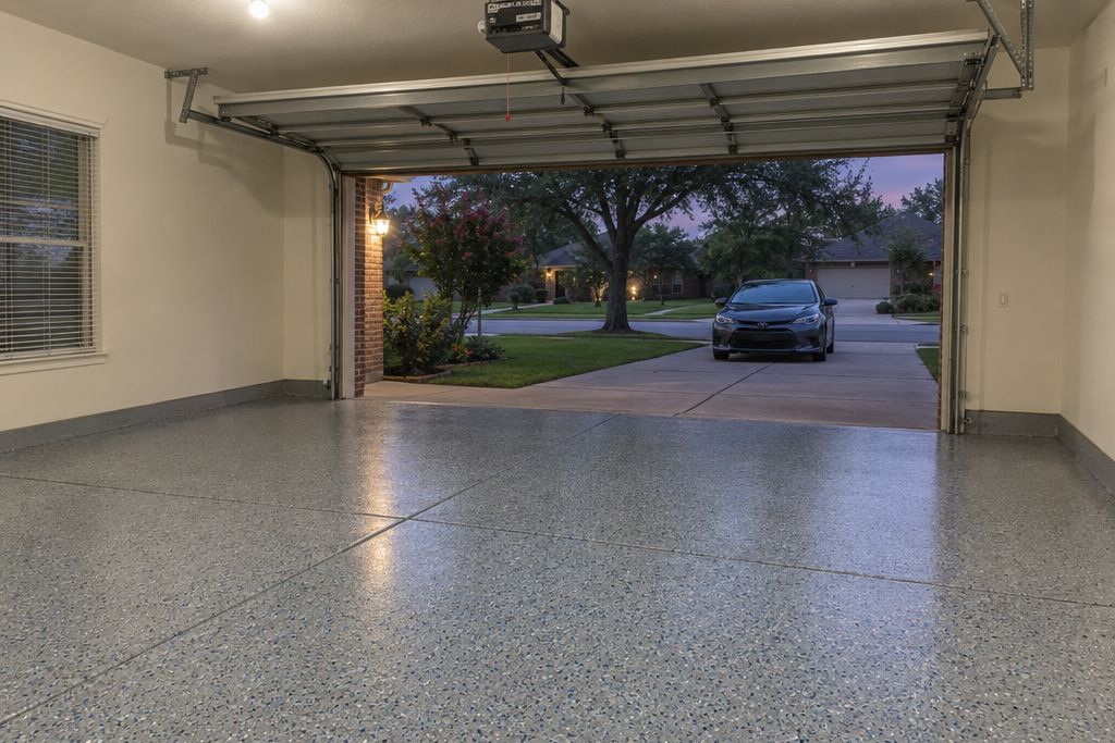Finished flake garage floor in the evening with the ceiling light on and a car waiting on the driveway beside the open door
