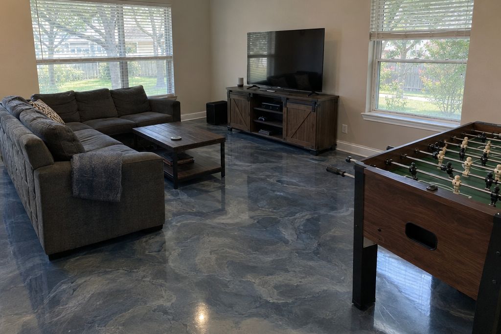 Game room on a house slab with a deep blue-gray metallic epoxy floor, a sofa and a television stand