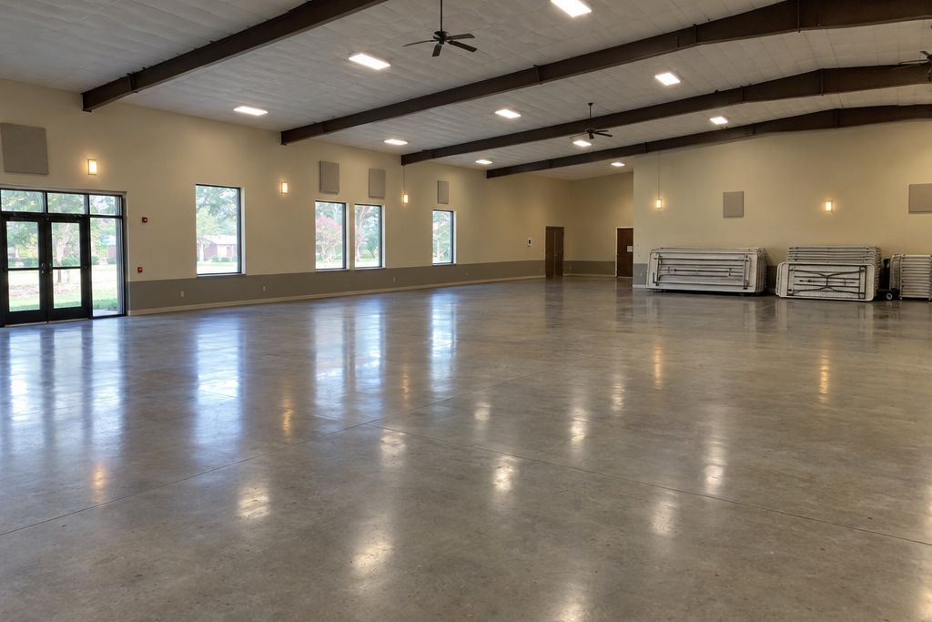Large empty event hall with a polished concrete floor reflecting the ceiling lights and folding tables stacked by a wall