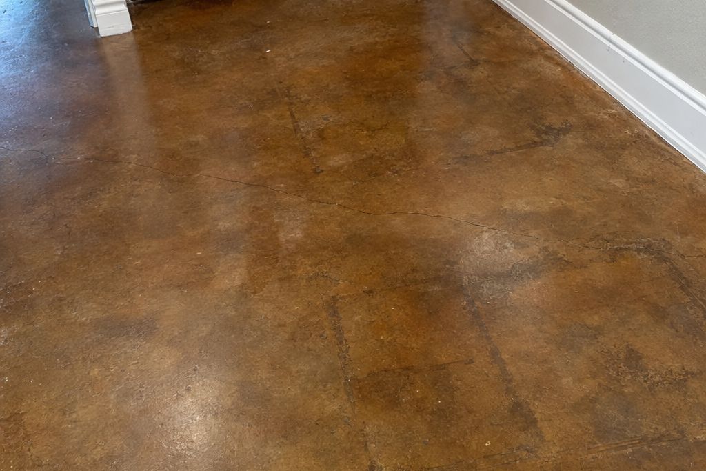 Stained concrete floor showing an old crack line and faint outlines of old adhesive under the brown stain
