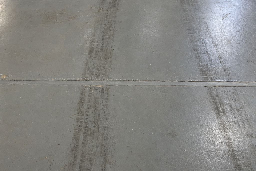 Close view of a warehouse floor control joint filled with gray joint filler, with faint forklift wheel tracks across the coated slab